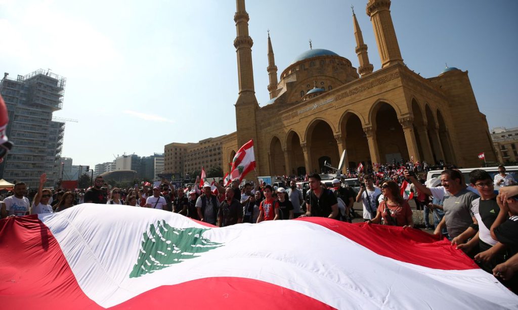 Manifestantes carregam bandeiras nacionais durante um protesto contra o governo no centro de Beirute, Líbano, em 20 de outubro de 2019 © ALI HASHISHO